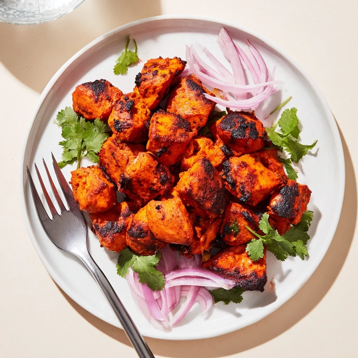Succulent Indian Tikka Spiced Chicken served on a platter with fresh cilantro and lemon wedges.