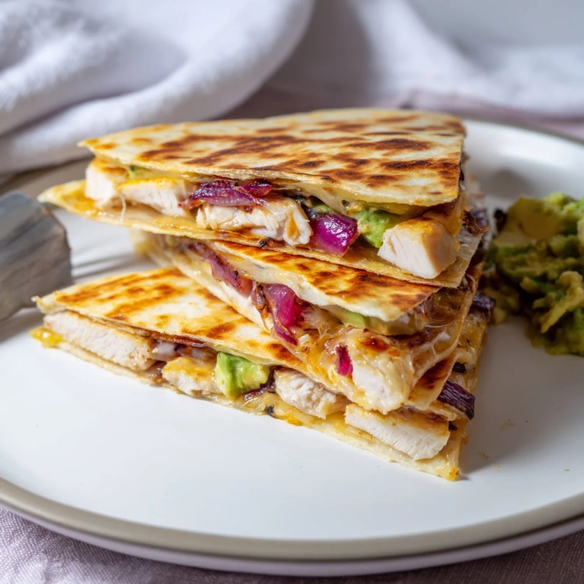 A close-up of a Chicken Avocado Quesadilla, its golden tortilla cut into wedges to reveal melted cheese, grilled chicken, and bright green avocado mash.