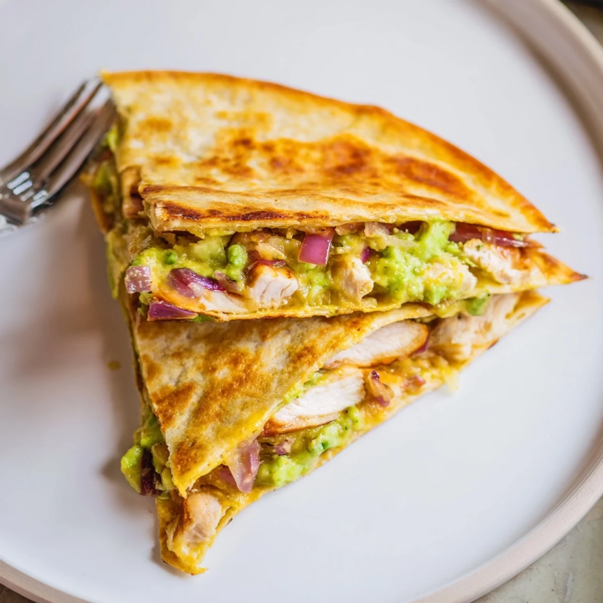 A hand holding a warm Chicken Avocado Quesadilla slice, showcasing the gooey cheese, juicy chicken, and creamy avocado filling inside.