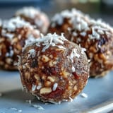 Twelve round Hojicha Energy Balls are arranged on a white plate with a glass of green tea for a calming Japanese-inspired snack pairing.