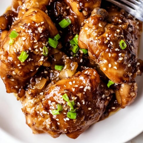 Golden-brown Honey Garlic Glazed Chicken thighs sizzling in a skillet, coated in a sticky, glossy sauce with flecks of garlic and red pepper flakes.