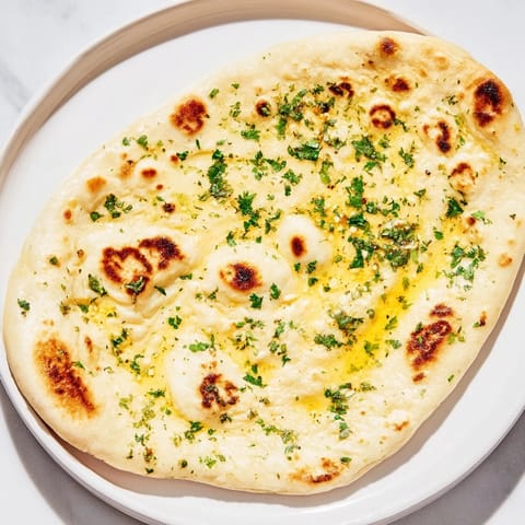 Warm, soft homemade garlic naan, with a generous brushing of flavorful garlic butter on top.