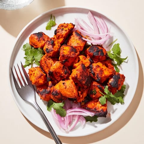Succulent Indian Tikka Spiced Chicken served on a platter with fresh cilantro and lemon wedges.