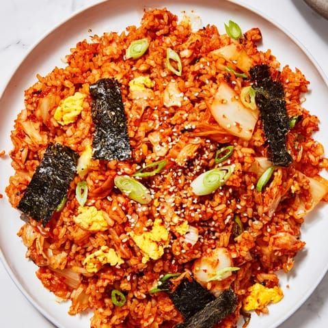 A close-up of spicy kimchi fried rice with fluffy grains, colorful veggies, and a sunny-side-up egg.