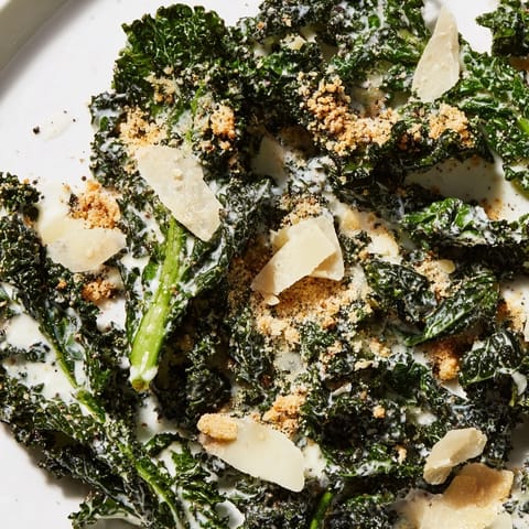 A freshly prepared Garlic Parmesan Kale Salad, served in a white bowl with shaved Parmesan and extra black pepper.  