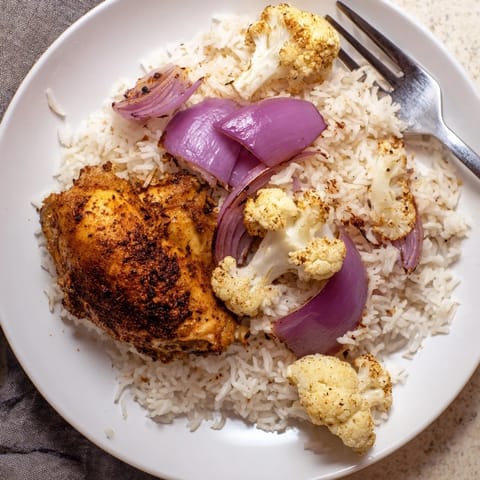 Freshly chopped parsley and lemon wedges garnish this savory roasted cauliflower chicken sheet pan served over fluffy rice.