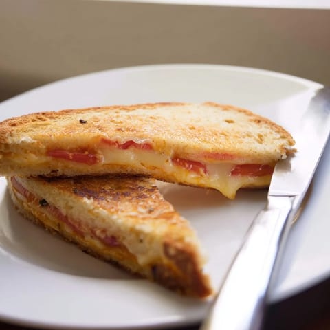 Close-up of a Pepper Jack & Tomato Grilled Cheese sliced in half, revealing gooey pepper jack and fresh tomato layers.