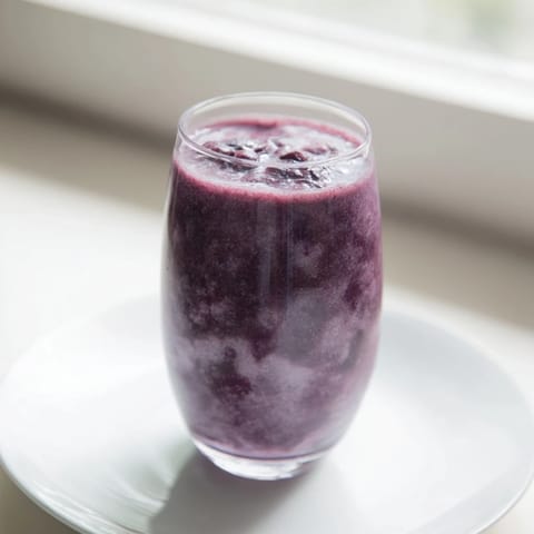 Two frosty glasses of Cherry Almond Smoothie beside whole cherries and almond butter on a wooden table.  
