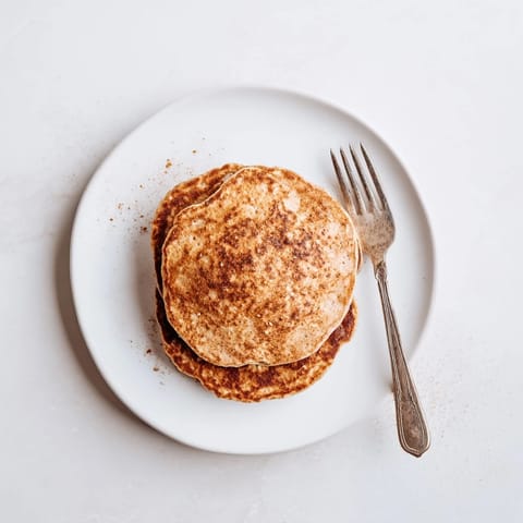 Stack of fluffy Banana Oat Pancakes served on a rustic plate with berries and a dollop of yogurt, highlighting their hearty, protein-rich texture.