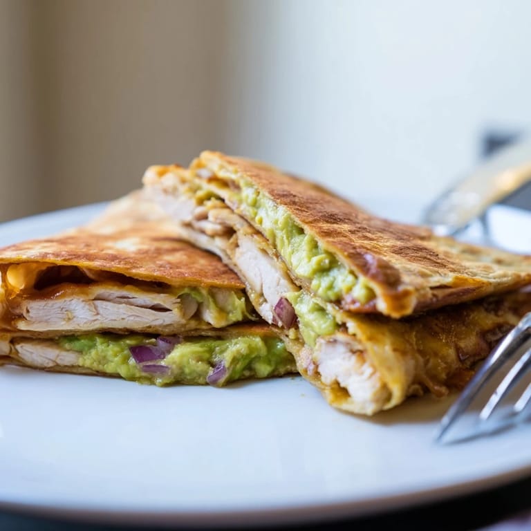 Golden-brown Chicken Avocado Quesadilla wedges stacked on a plate, with a side of creamy salsa for dipping and a fresh lime wedge.