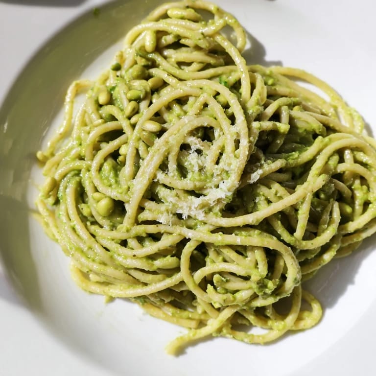 A comforting serving of Sunflower Seed Pesto Pasta with bright lemon notes, creamy sauce clinging to each bite, and a sprig of fresh basil.