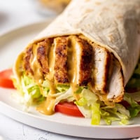 Golden-brown honey mustard chicken tenders nestled in a soft tortilla with crisp lettuce and fresh tomato slices.