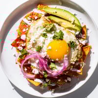 Crispy corn tortilla chips coated in vibrant salsa verde, topped with a runny fried egg and fresh cilantro garnish.  