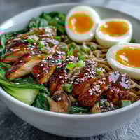 A close-up of Healthy Miso Chicken Noodle Bowls with sliced chicken, soft-boiled egg, and bok choy in savory broth.